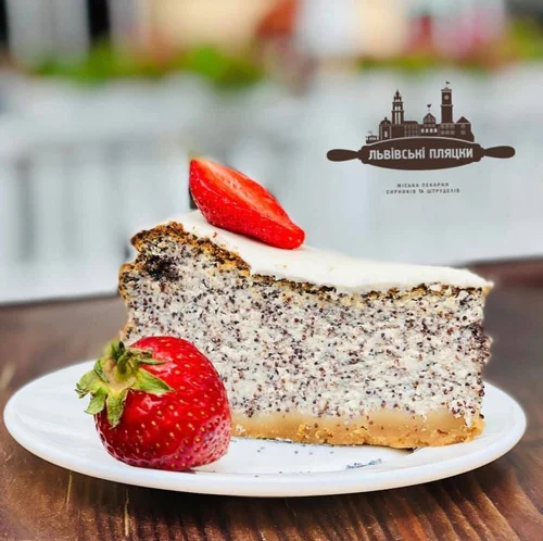 A slice of poppy seed cake with a layer of white frosting, garnished with a sliced strawberry on top and a whole strawberry on the plate, on a white dish.