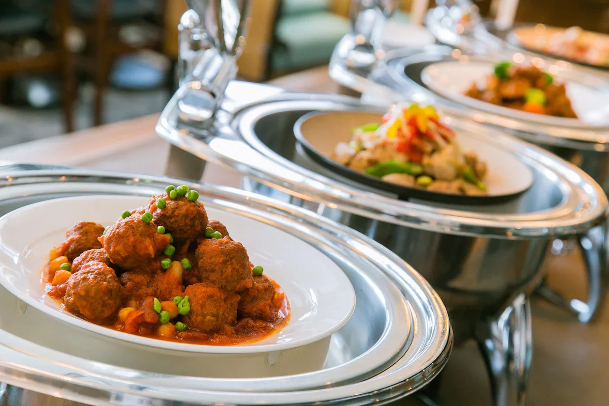 Chafing dishes with meatballs and colorful salad at a buffet restaurant.