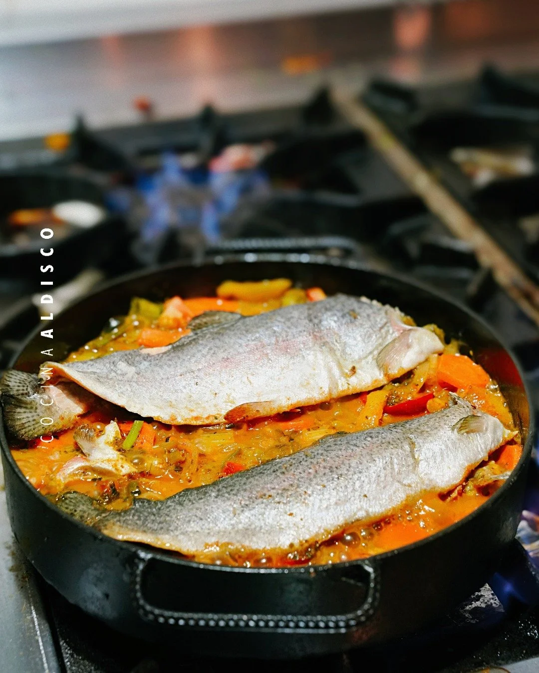 Two whole fish cooking on a skillet with vegetables in a kitchen stove.