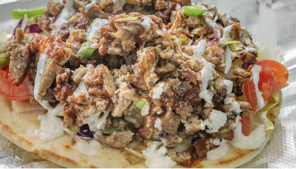 Close-up of a taco with seasoned ground beef, shredded lettuce, tomato slices, and creamy white sauce