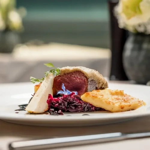 A plated gourmet meal featuring a portion of cooked meat wrapped in pastry, with side dishes of mashed potatoes, mixed berries, and garnished with a sprig of rosemary.