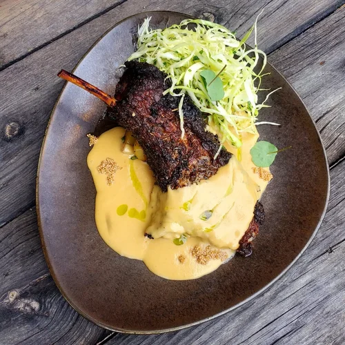 Grilled meat skewer with creamy sauce, served with shredded cabbage salad on a dark ceramic plate on a wooden table.