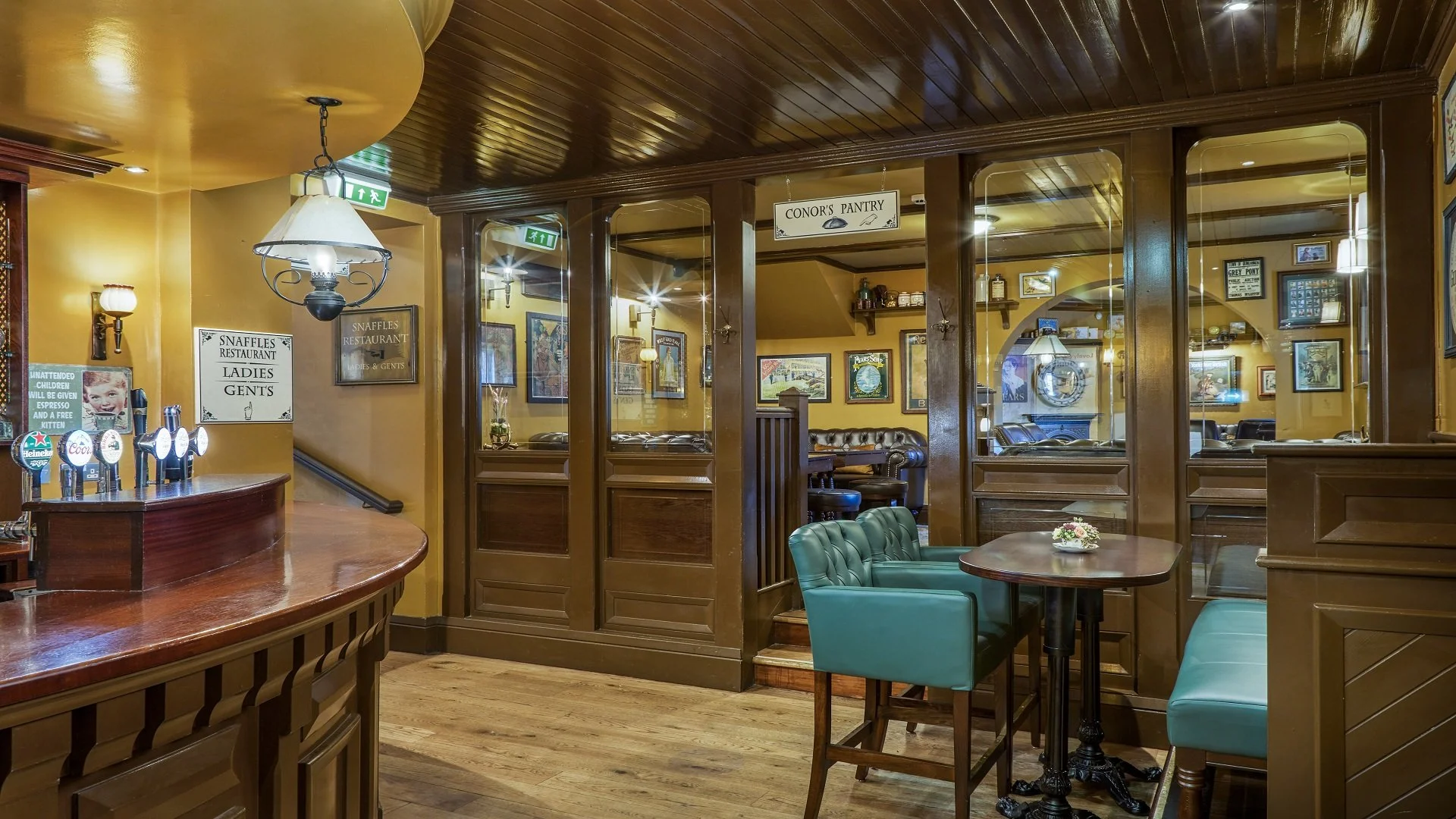 Interior of a cozy pub or restaurant with wooden accents, green upholstered chairs, a small round table, and wall decor.