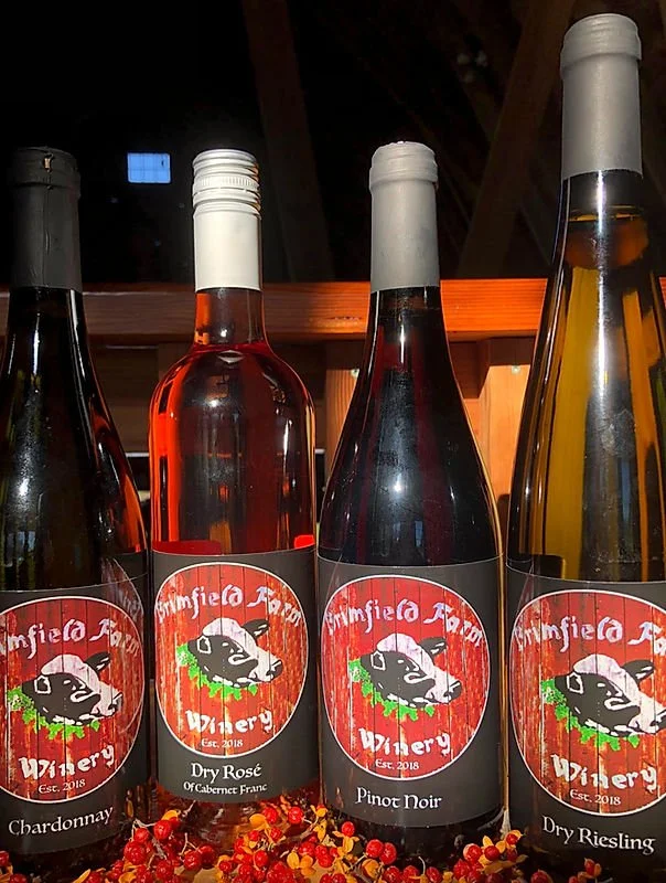 Four bottles of wine from Kimfield Farm Winery in a row, including Chardonnay, Dry Rosé, Pinot Noir, and Dry Riesling, with some red berries in front.