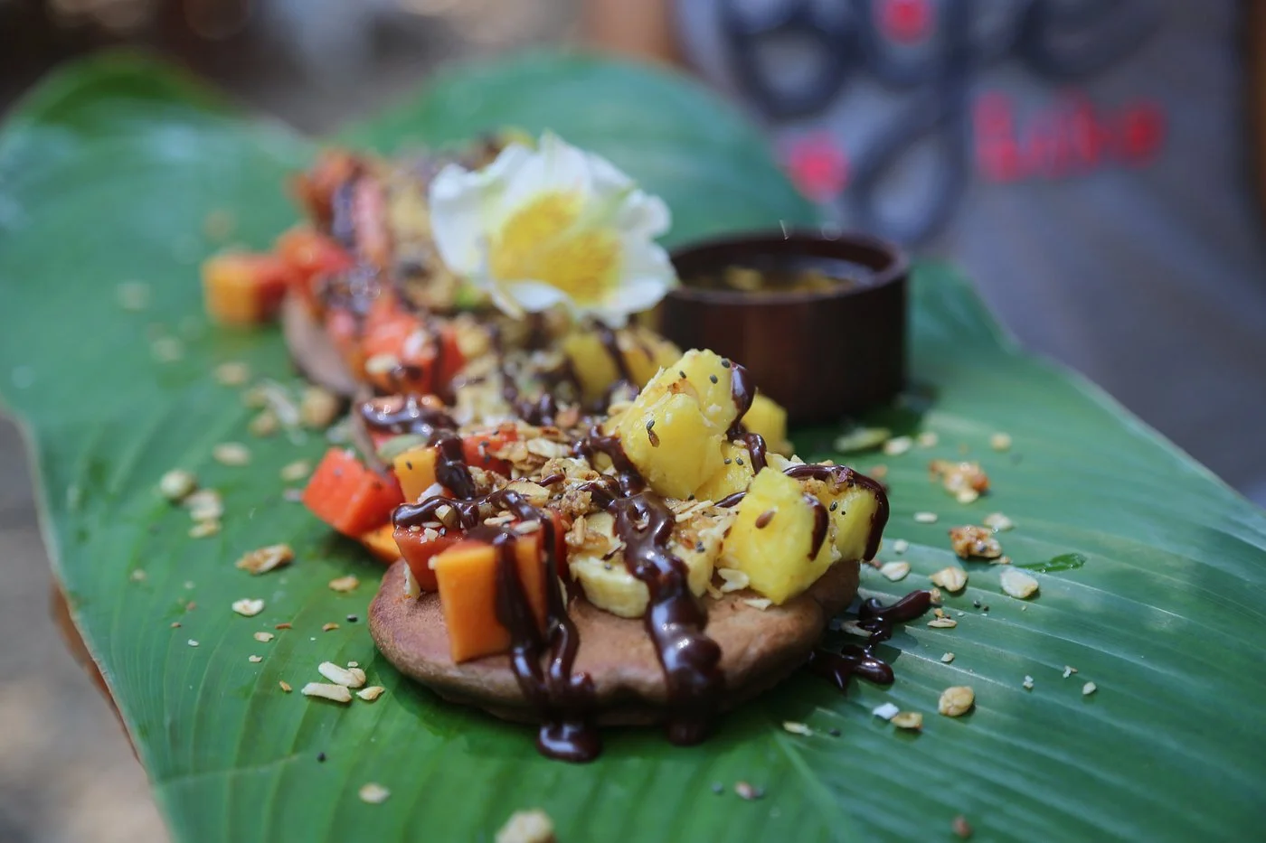 A plate of tostones topped with fruit, chocolate, and a flower on a banana leaf