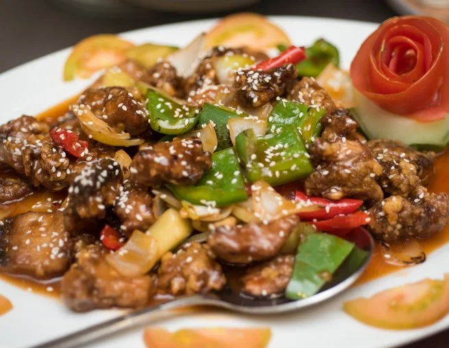 Sweet and sour chicken with green bell peppers, onions, and red peppers served with a carved cucumber and tomato garnish.