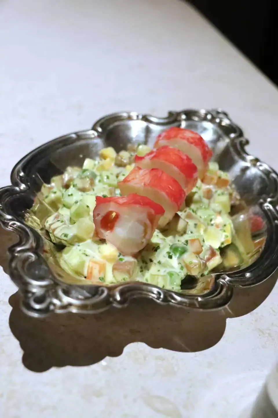 A silver decorative bowl containing a salad with imitation crab meat on top.