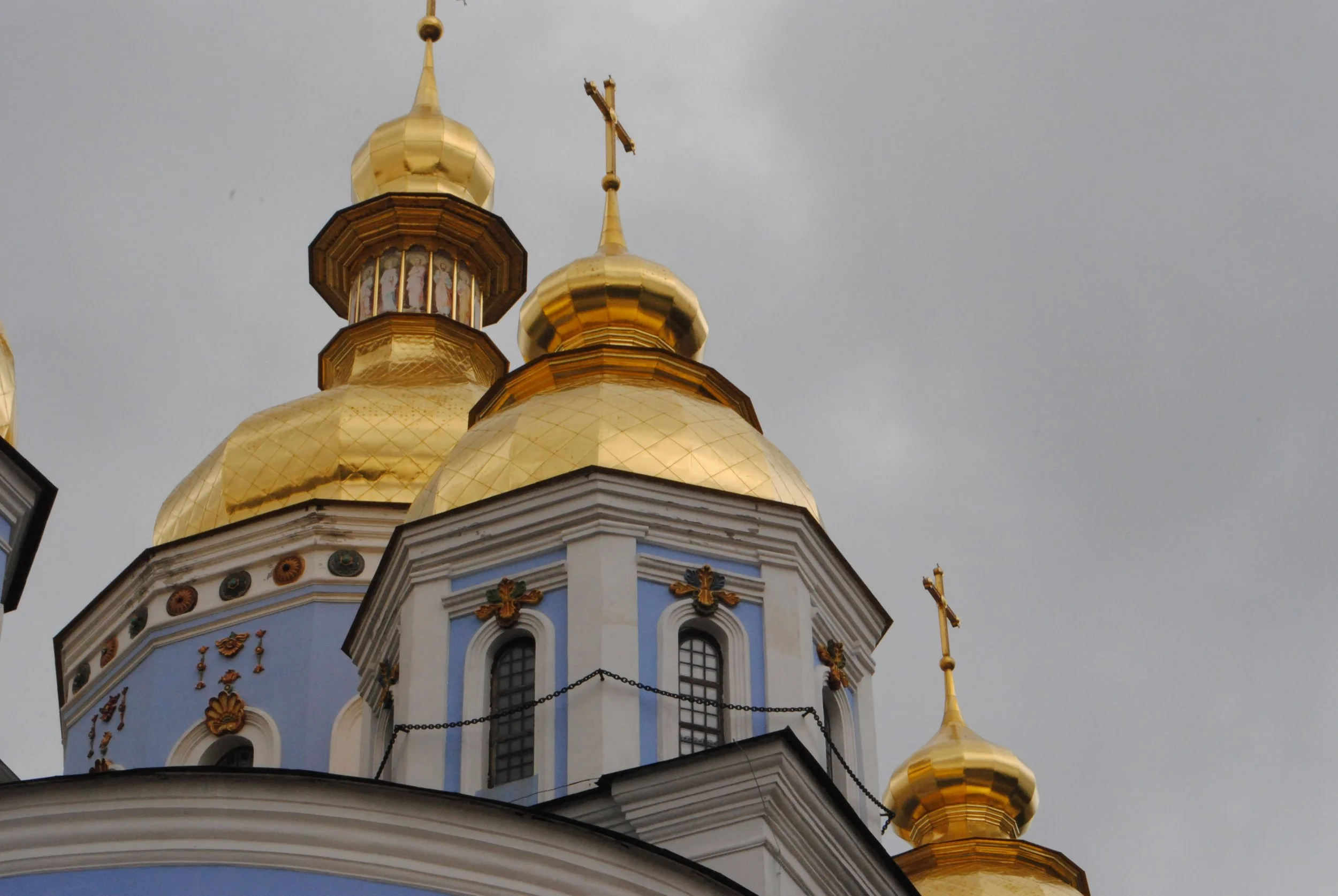 Close-up of an ornate church with blue walls, golden domes, and crosses against a cloudy sky.
