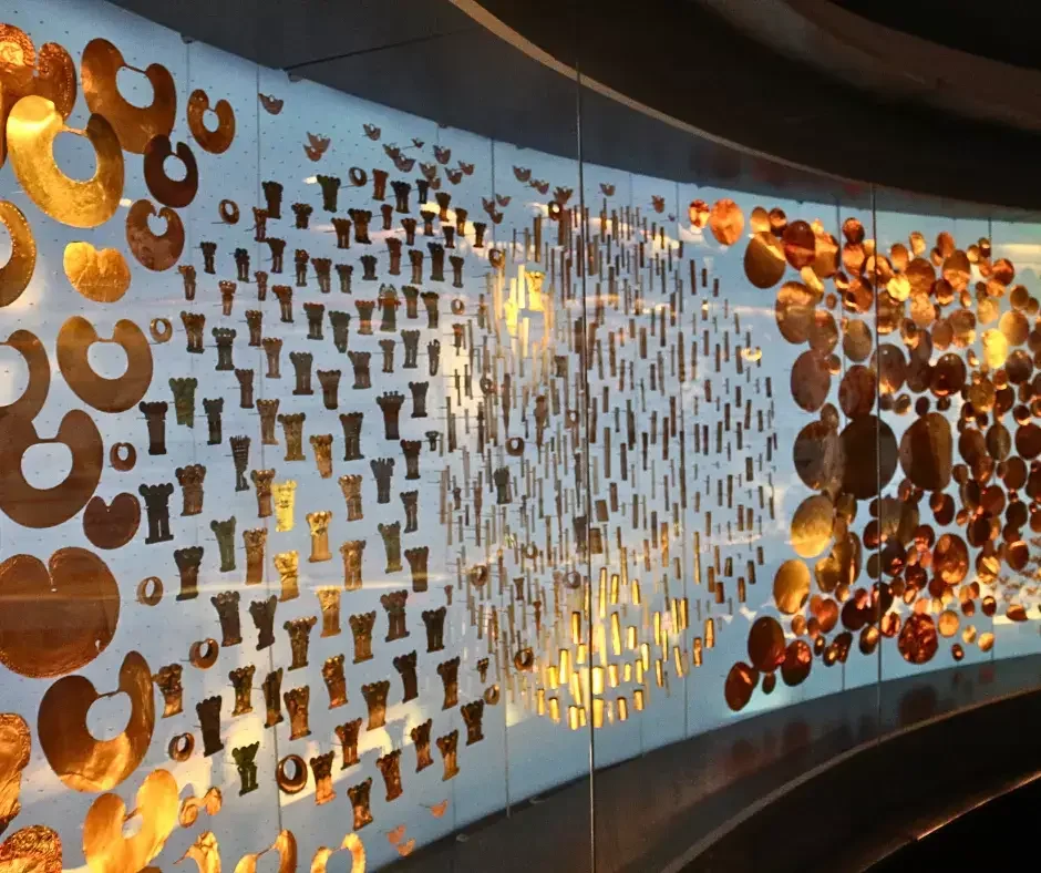Decorative metal art installation with a large heart shape in the center, surrounded by various circular and cylindrical gold-colored metal pieces on a glass wall.