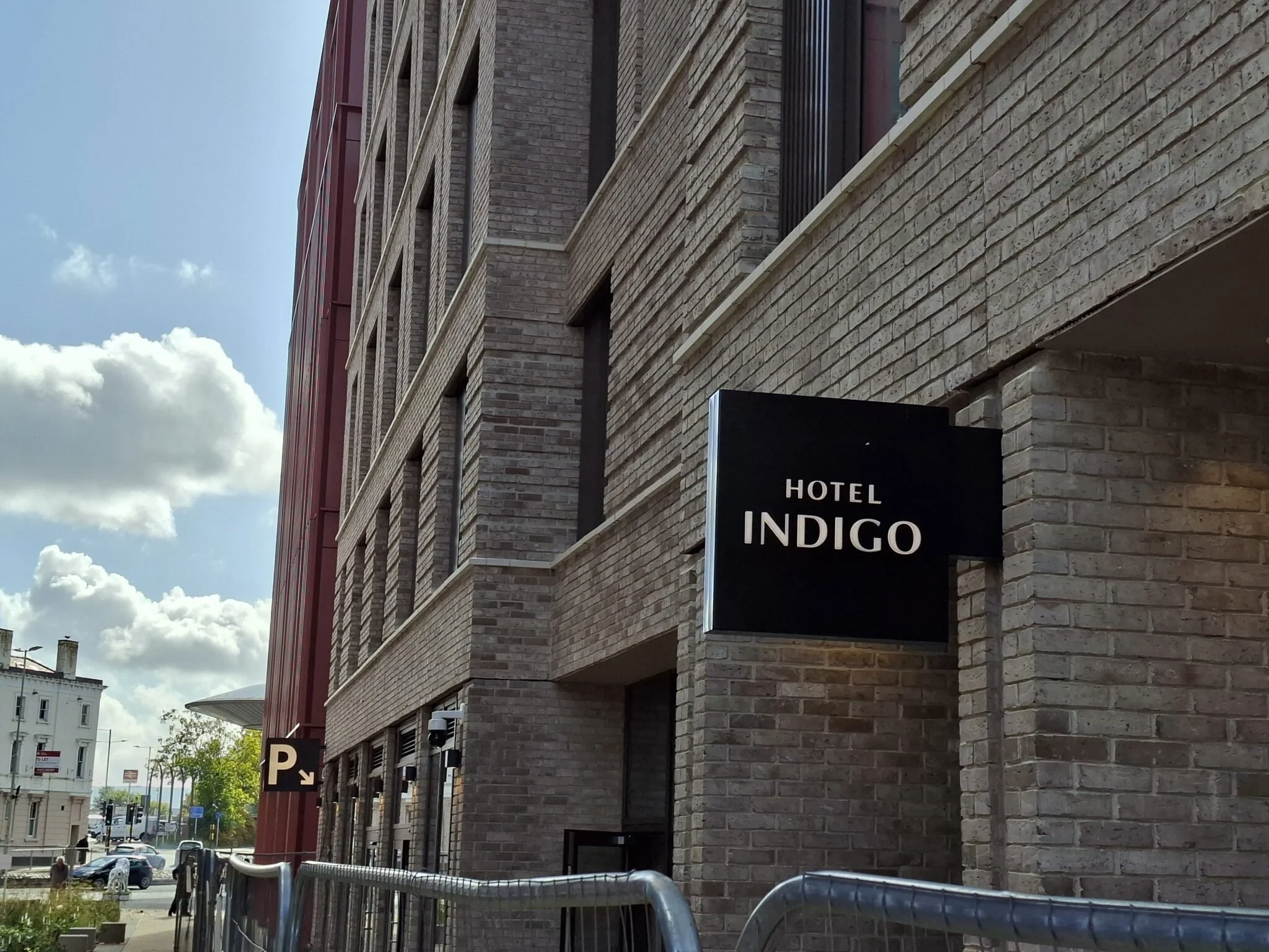 A brick building with a sign that reads "Hotel Indigo" on the exterior wall, with a parking sign and some cars parked on the street.