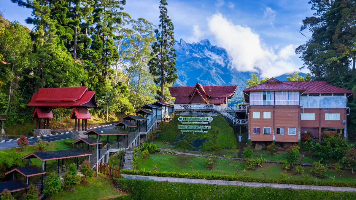 A scenic view of a hillside with multiple traditional-style buildings with red roofs, surrounded by lush green trees and mountains in the background.
