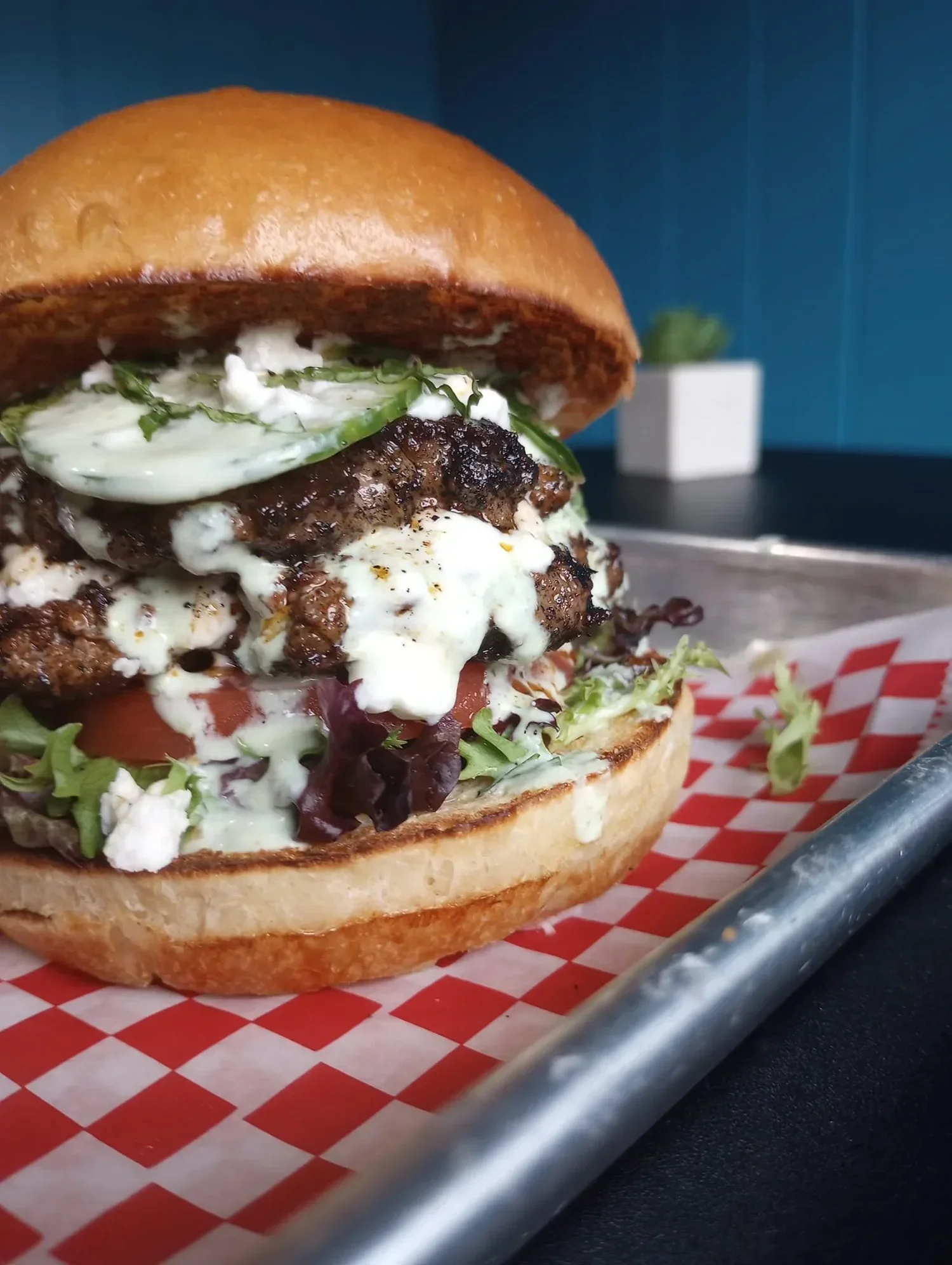 Close-up of a hamburger with beef patty, lettuce, tomato, cheese, and sauce in a toasted bun, served on a paper-lined tray.