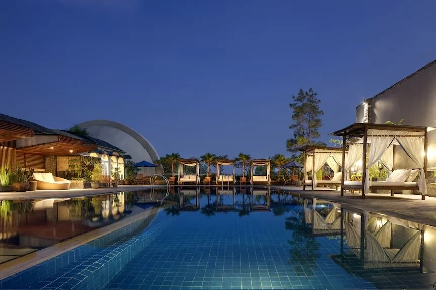 Luxury poolside area with lounge chairs and cabanas at dusk, reflecting in the pool water.