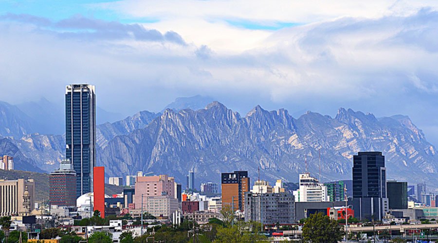 City skyline with tall buildings and mountains in the background under a partly cloudy sky.