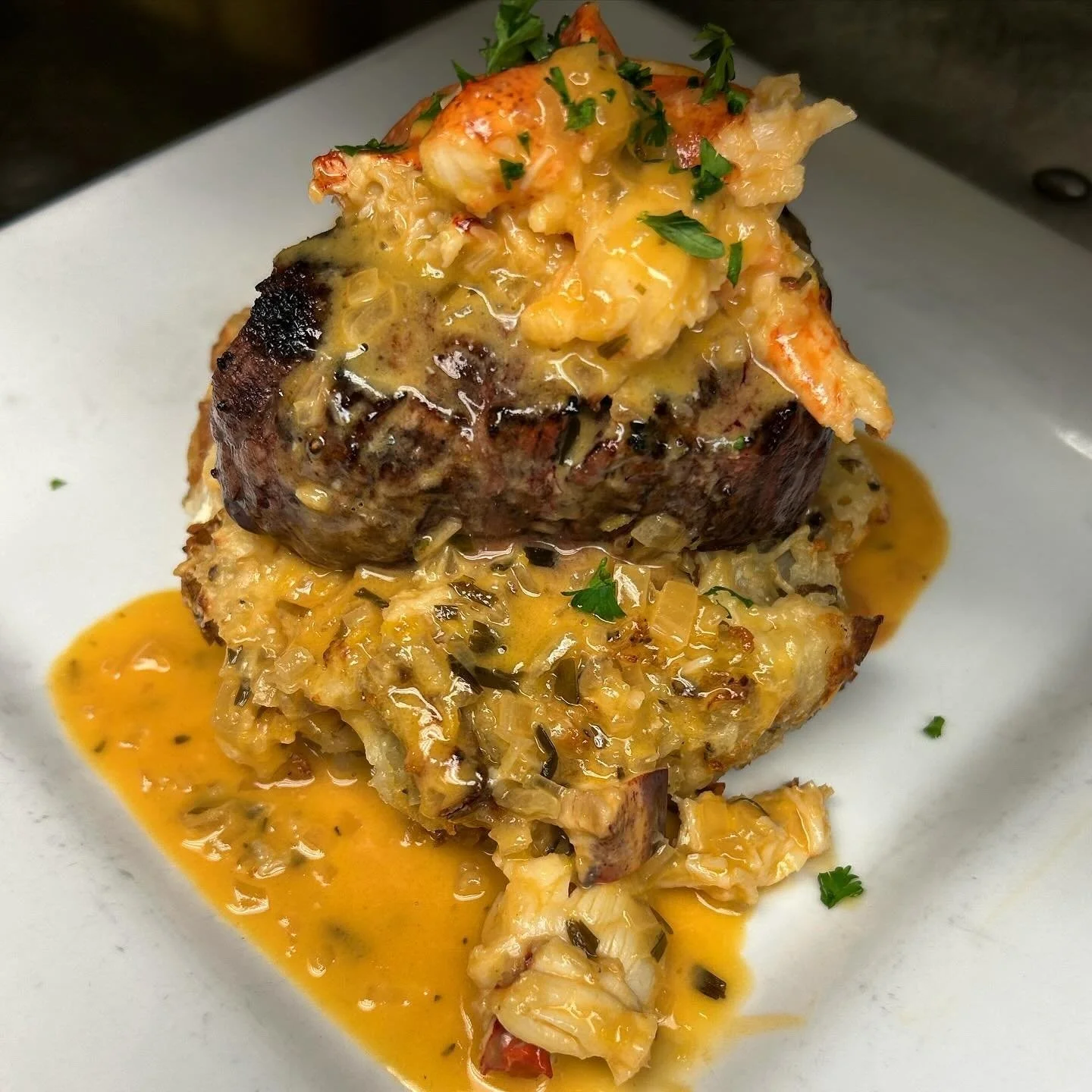 A serving of filet mignon topped with lobster and melted cheese, served with roasted potatoes and vegetables.