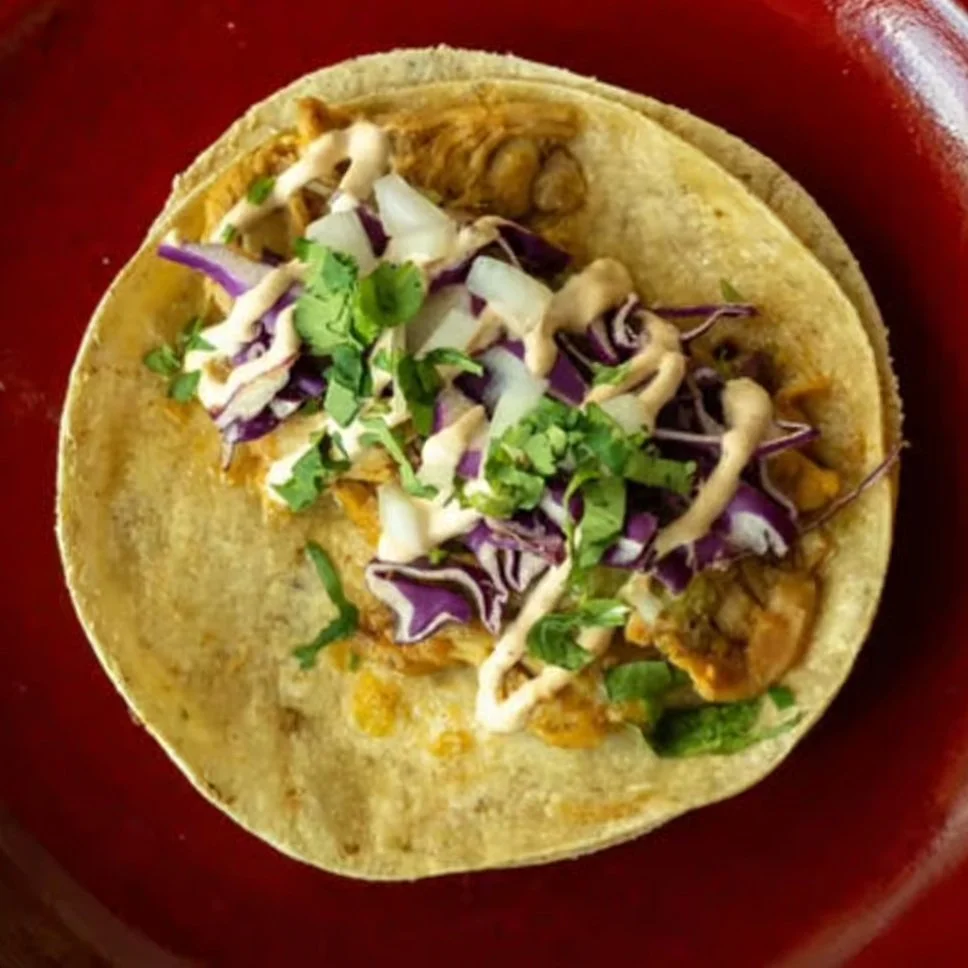 Close-up of a taco in a red bowl with shredded lettuce, chopped onions, and cilantro.