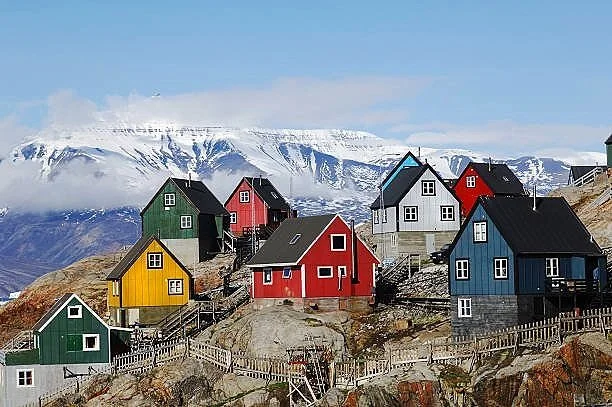 Colorful houses built on a rocky slope with snow-covered mountains in the background.