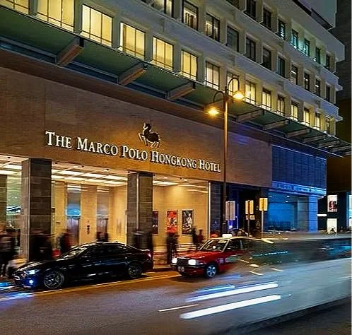 Night view of The Marco Polo Hongkong Hotel entrance with cars on the street, illuminated signage, and a multi-story building with windows above.