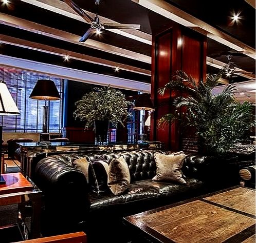 Luxurious hotel lobby with leather sofa, decorative pillows, large potted plants, ambient lighting, and ceiling fans.