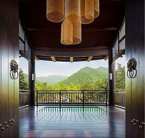 View from a covered wooden balcony overlooking green mountains with a railing and decorative lion head door knockers.