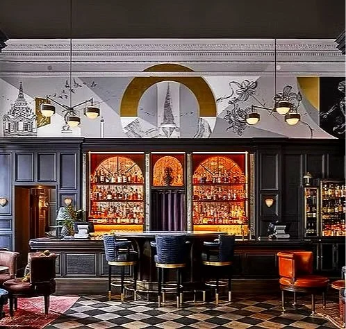 Elegant bar with black cabinetry, illuminated liquor shelves, a marble countertop, and a mirrored back wall with artistic decorations and lighting fixtures.