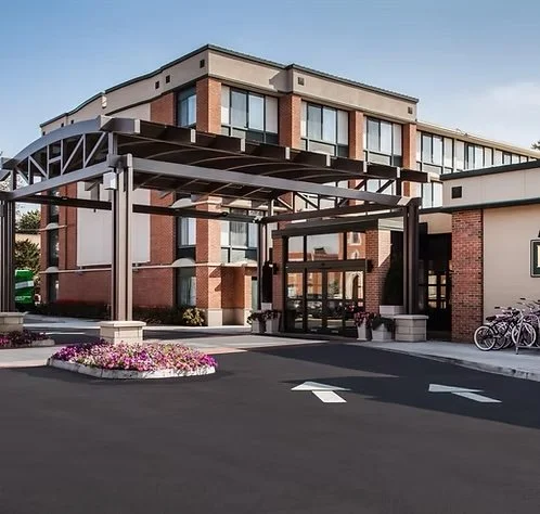 Modern hotel entrance with covered drop-off area, landscaped flower bed, and bicycles parked outside.