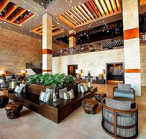 Luxury hotel lobby with a central planter, seating areas, and wooden ceiling accents.