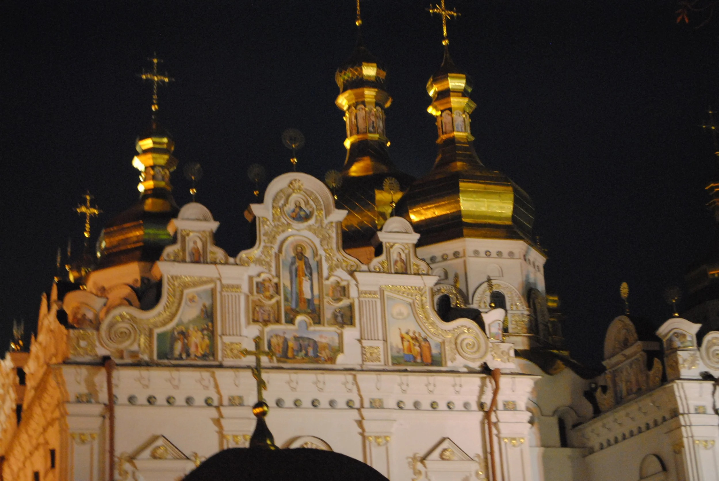 Nighttime view of an ornate church with multiple gold domes and crosses, decorated with religious icons and intricate gold detailing.