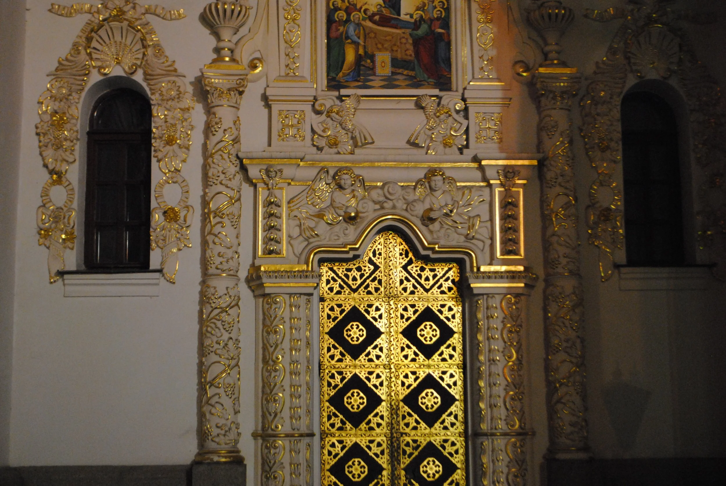 A richly decorated altar with intricate gold and white detailing, featuring angels, relief sculptures, and a religious painting above, set in a church.