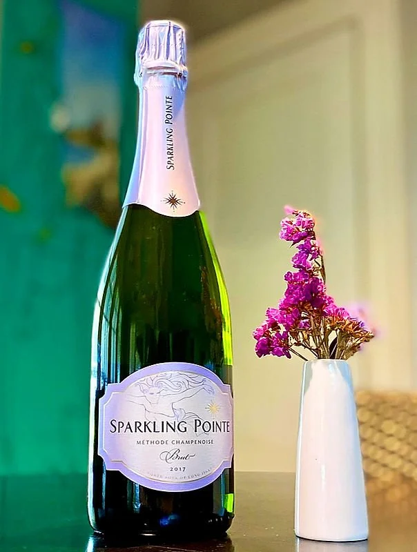A bottle of Sparkling Pointe champagne and a small white vase with pink flowers on a dark surface.