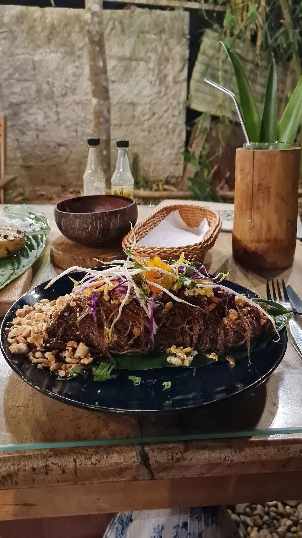 A plate of Asian-style shredded beef with noodles, garnished with bean sprouts, chopped peanuts, and herbs, served on a black plate on a wooden table.