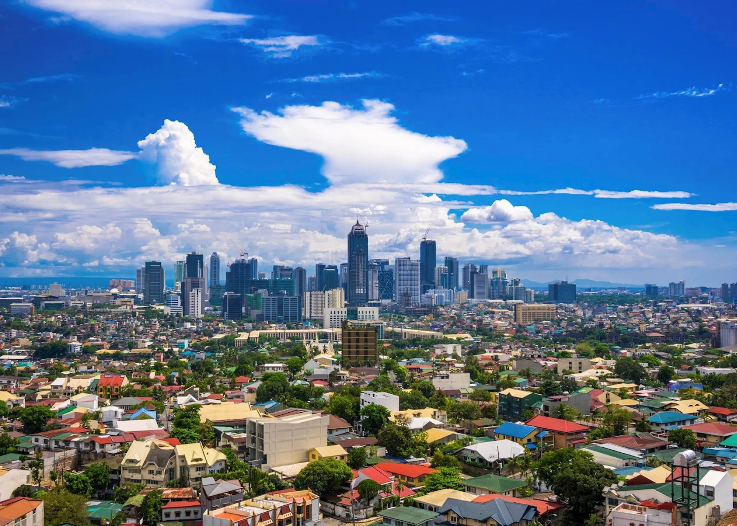 City skyline with tall buildings under a blue sky filled with scattered clouds.
