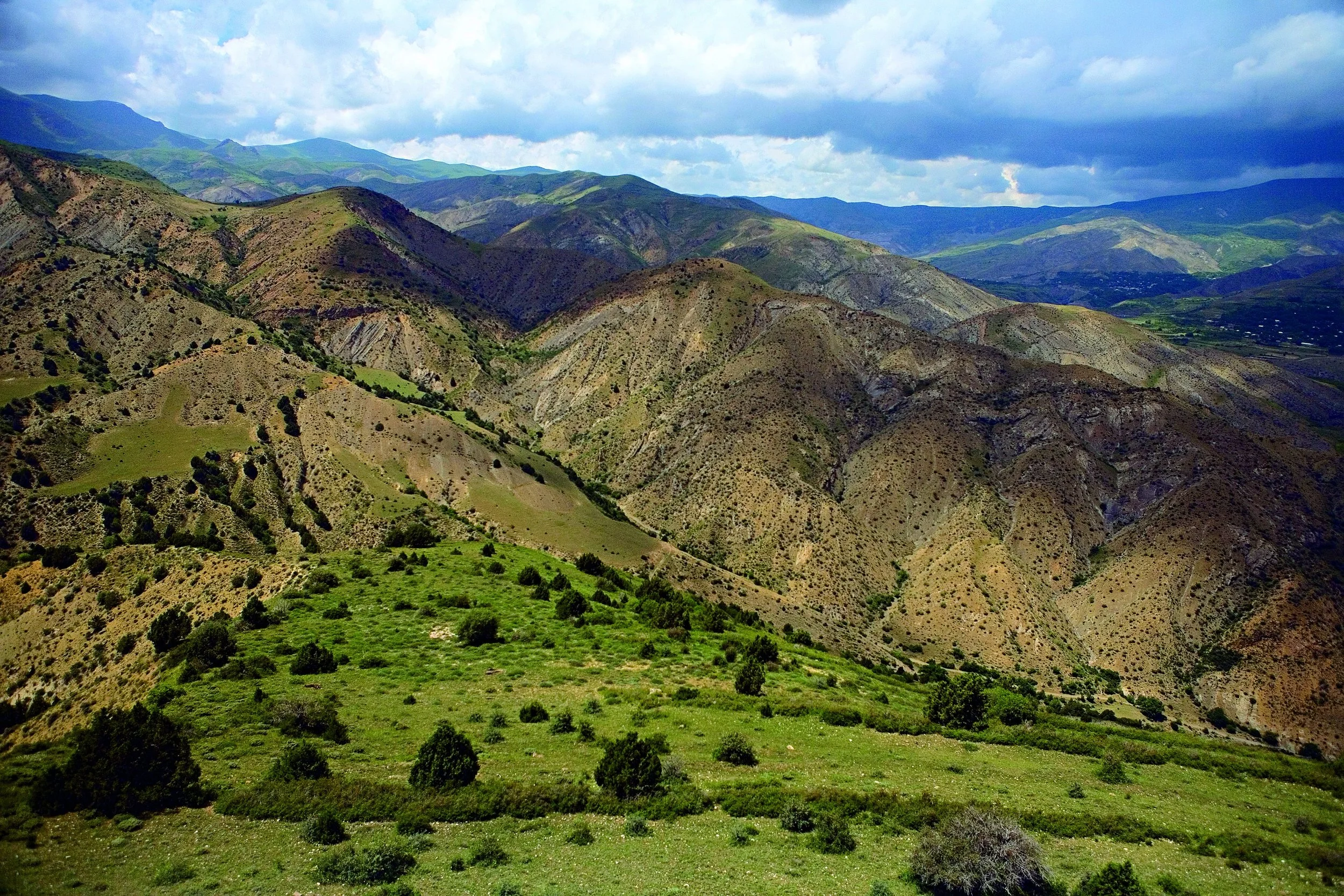 Rolling green hills and mountains under a partly cloudy sky.