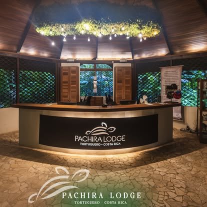 Reception desk at Pachira Lodge, Tortuguero, Costa Rica, with a illuminated sign and green foliage decoration overhead.