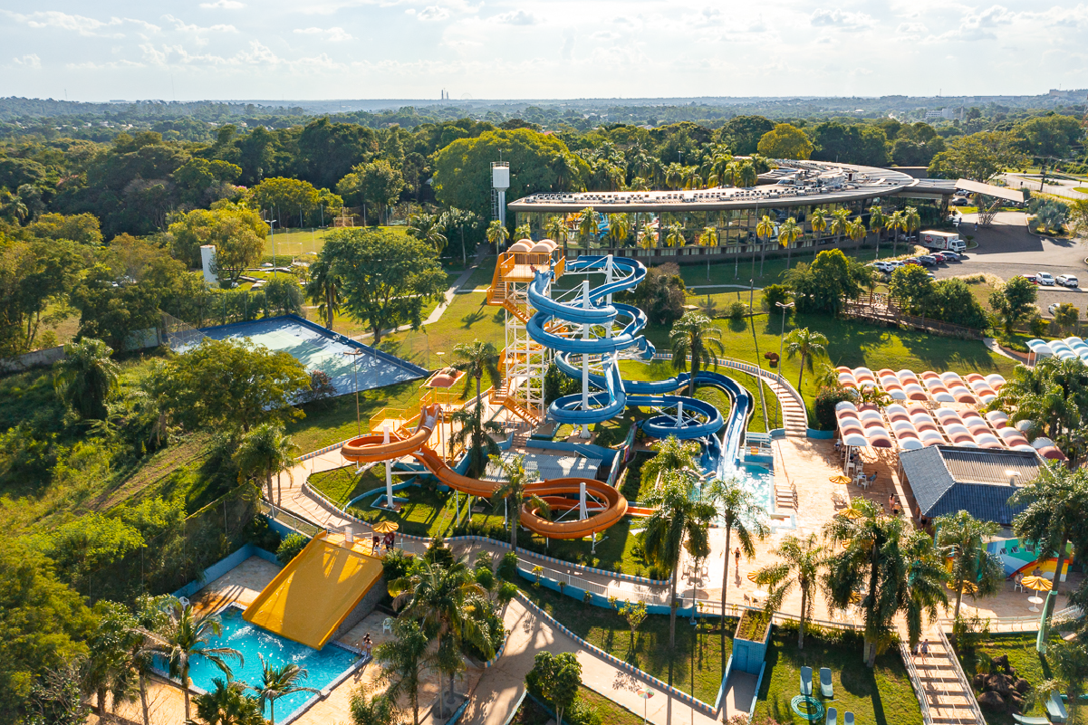Aerial view of a water park with multiple water slides, a swimming pool, and surrounding greenery under a partly cloudy sky.