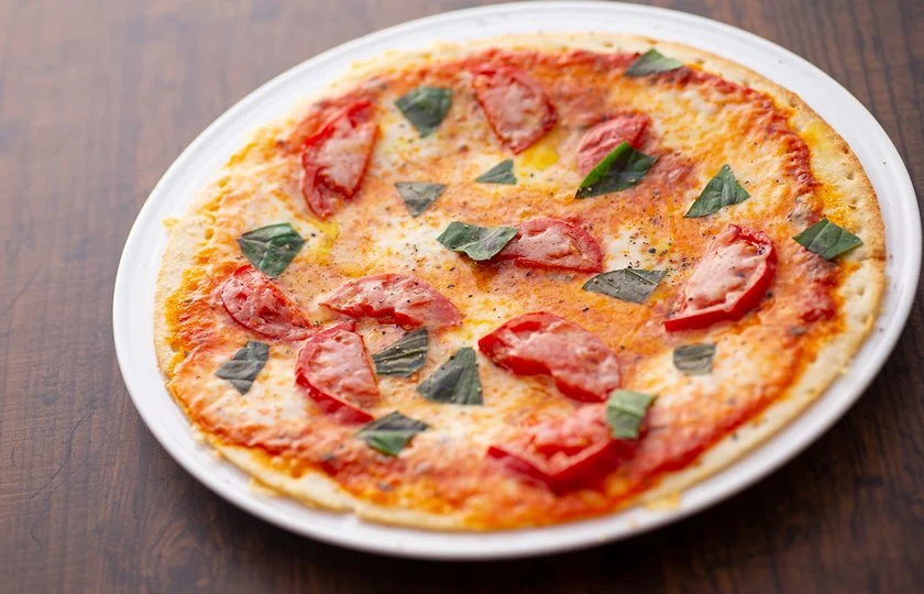 A pepperoni and basil pizza on a white plate placed on a wooden table.