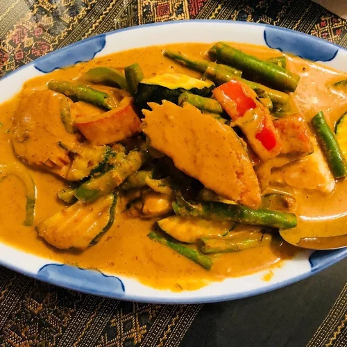A dish of vegetable curry with zucchini, green beans, red bell peppers, and curry sauce in a white and blue oval bowl.