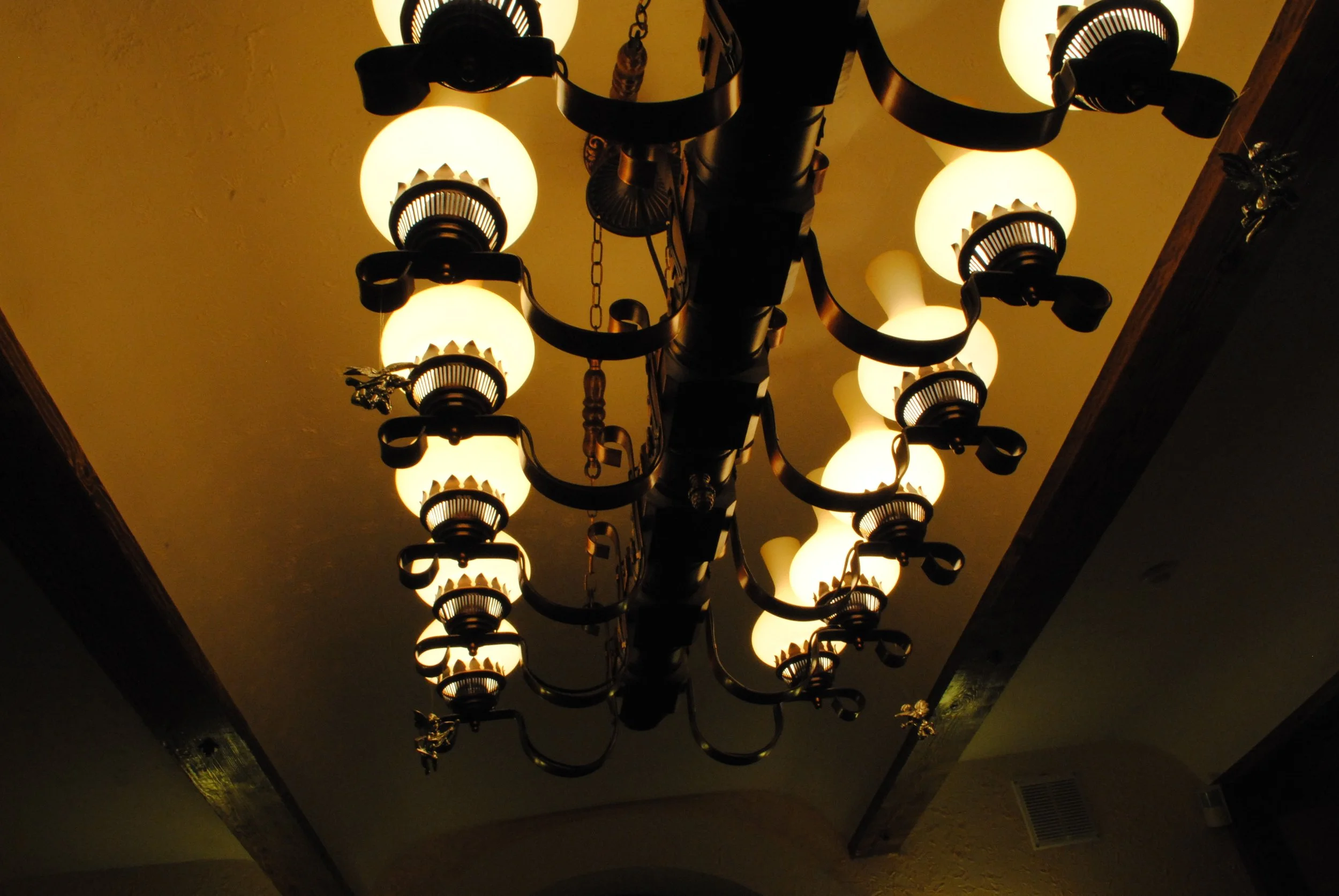 A large chandelier with multiple round, white lampshades hanging from the ceiling in a dimly lit room.