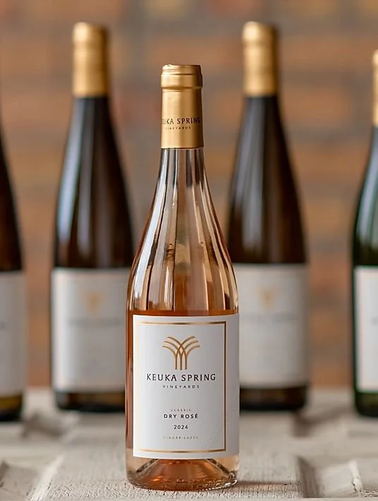 A bottle of Keuka Spring Vineyard's Classic Dry Rosé wine from 2024, with three additional bottles in the background on a wooden surface.