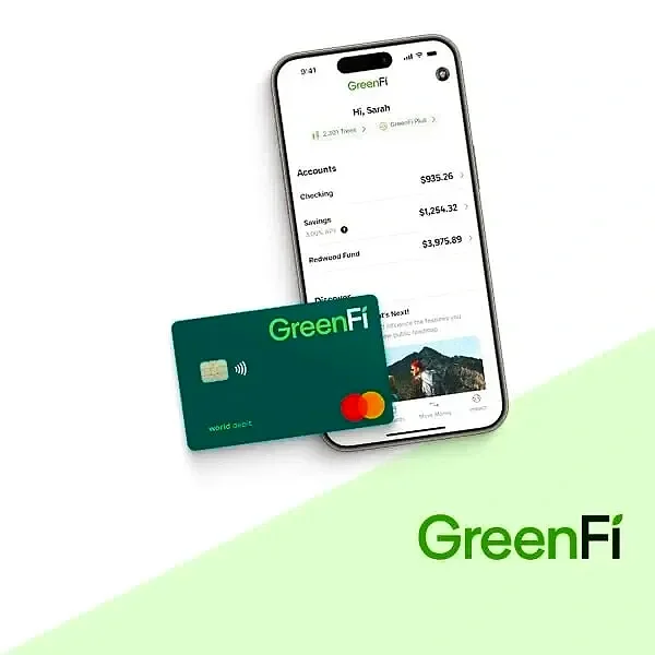 Two small dogs running on grass, one holding a tennis ball in its mouth, with trees and a blurred background.