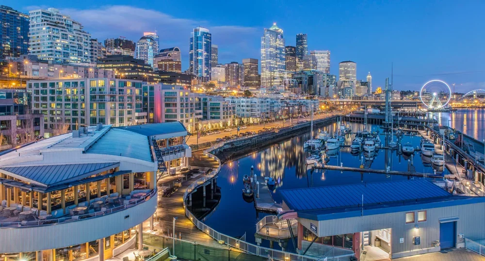 Seattle skyline at dusk with illuminated buildings, a Ferris wheel, and a marina with boats in the foreground.
