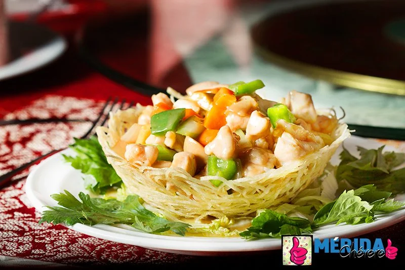 Close-up of a crab salad served in a crispy taco shell on a white plate, garnished with lettuce leaves, on a red tablecloth.