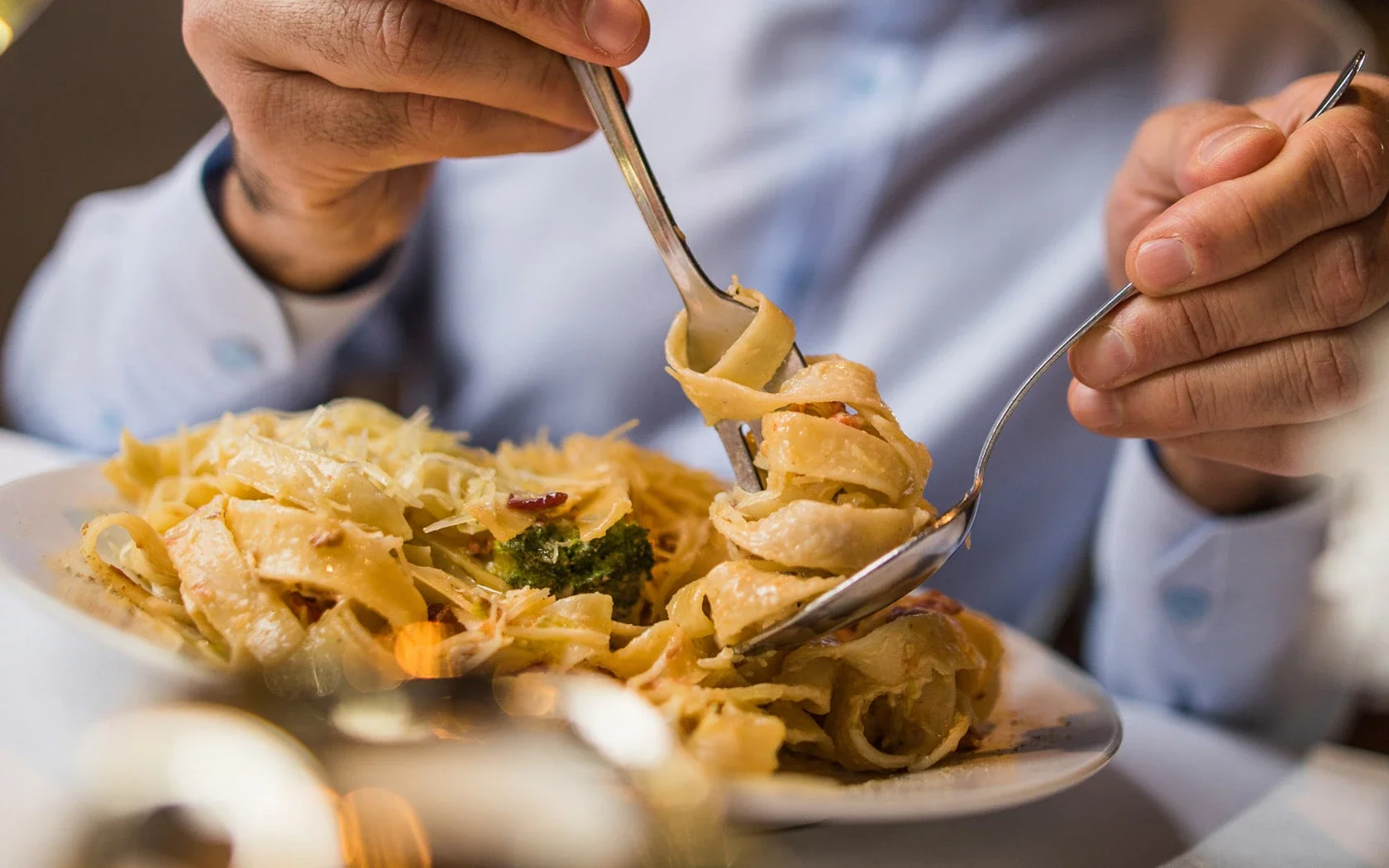 Person eating a plate of fettuccine pasta with broccoli and a creamy sauce.