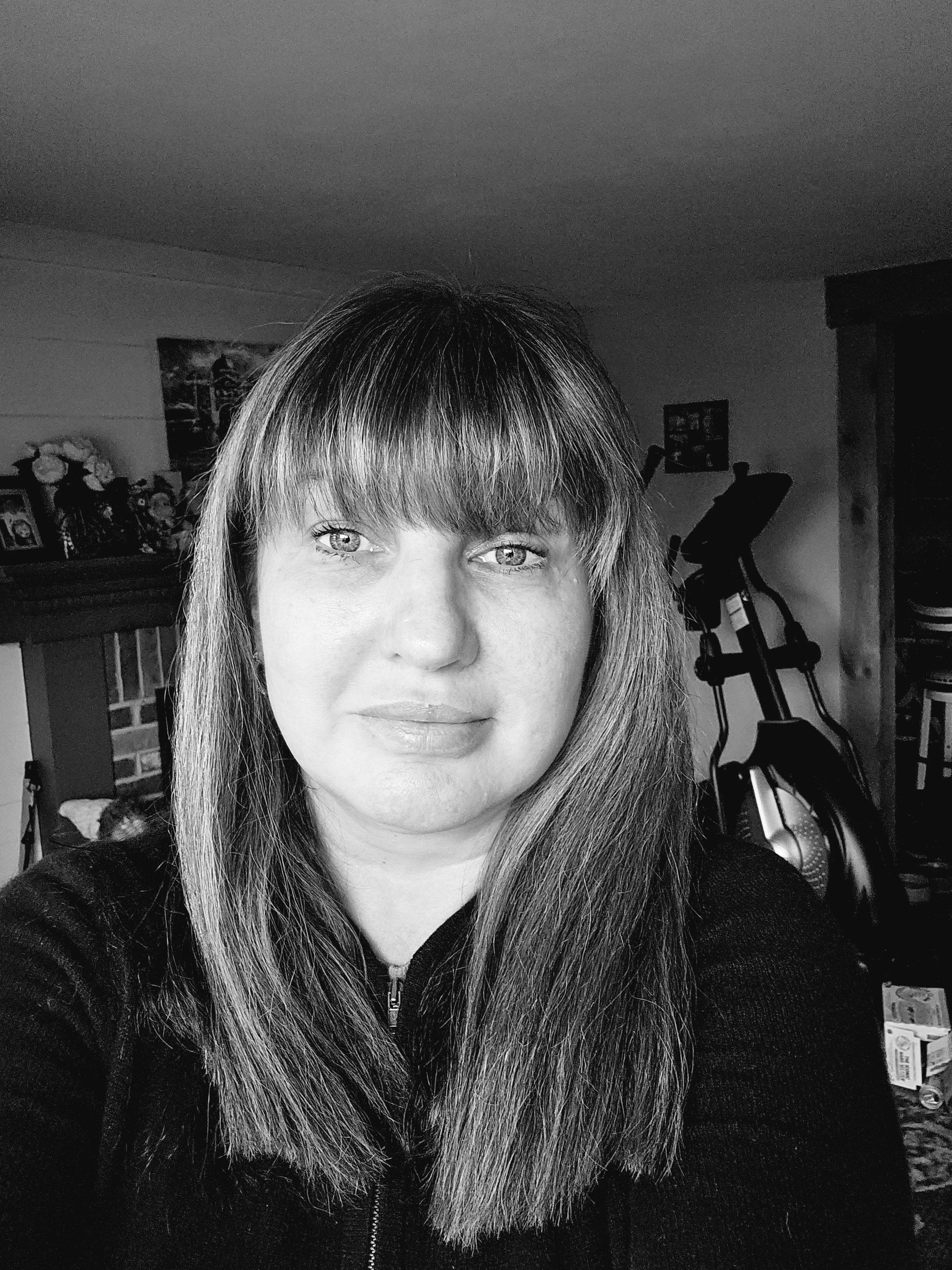 Black and white photo of a woman with long, straight hair and bangs, looking directly at the camera.