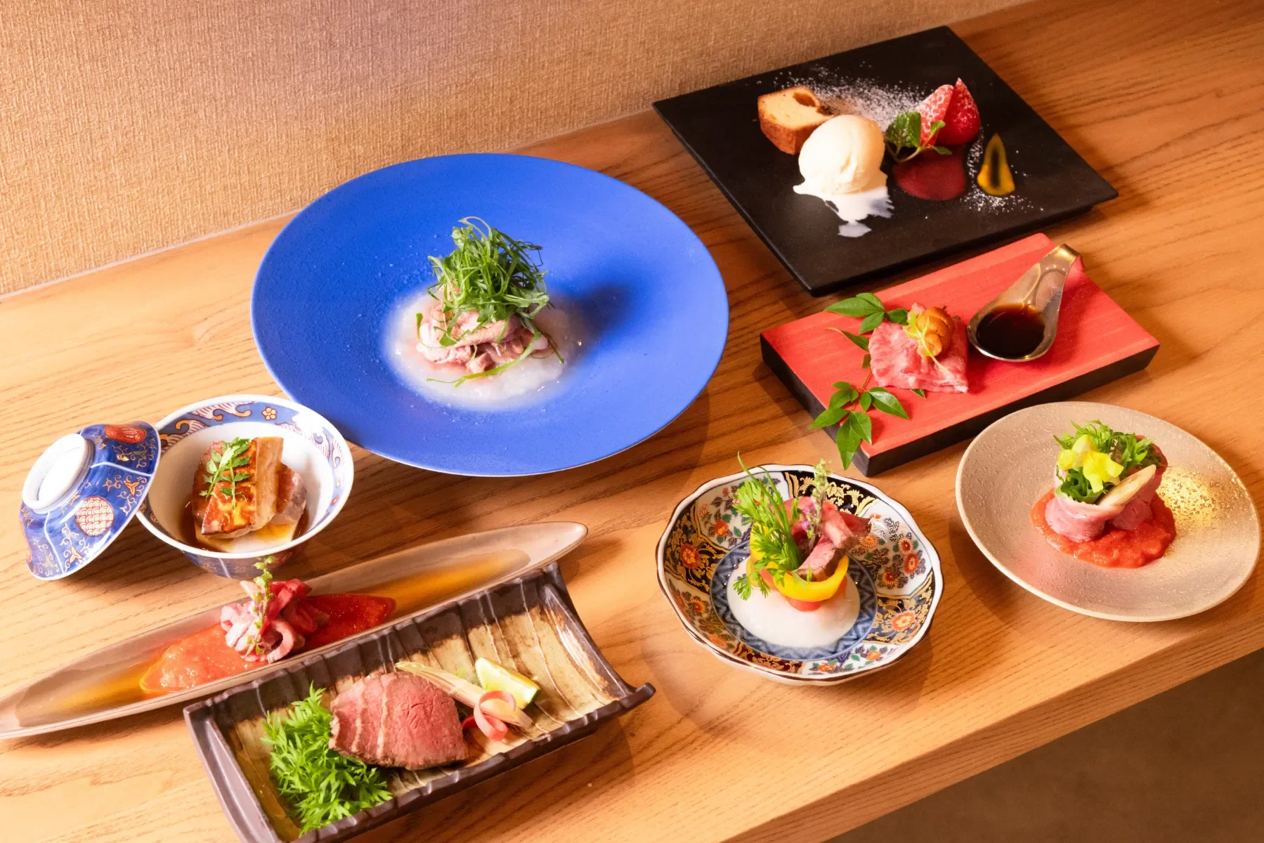 A table with an assortment of Japanese dishes, including sashimi, grilled meats, desserts, and various garnishes and sauces in decorative bowls and plates.