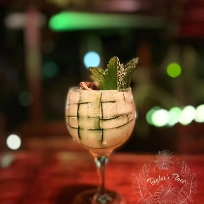 Cocktail in a glass garnished with green herbs, set against a blurred, colorful background with bokeh lights.