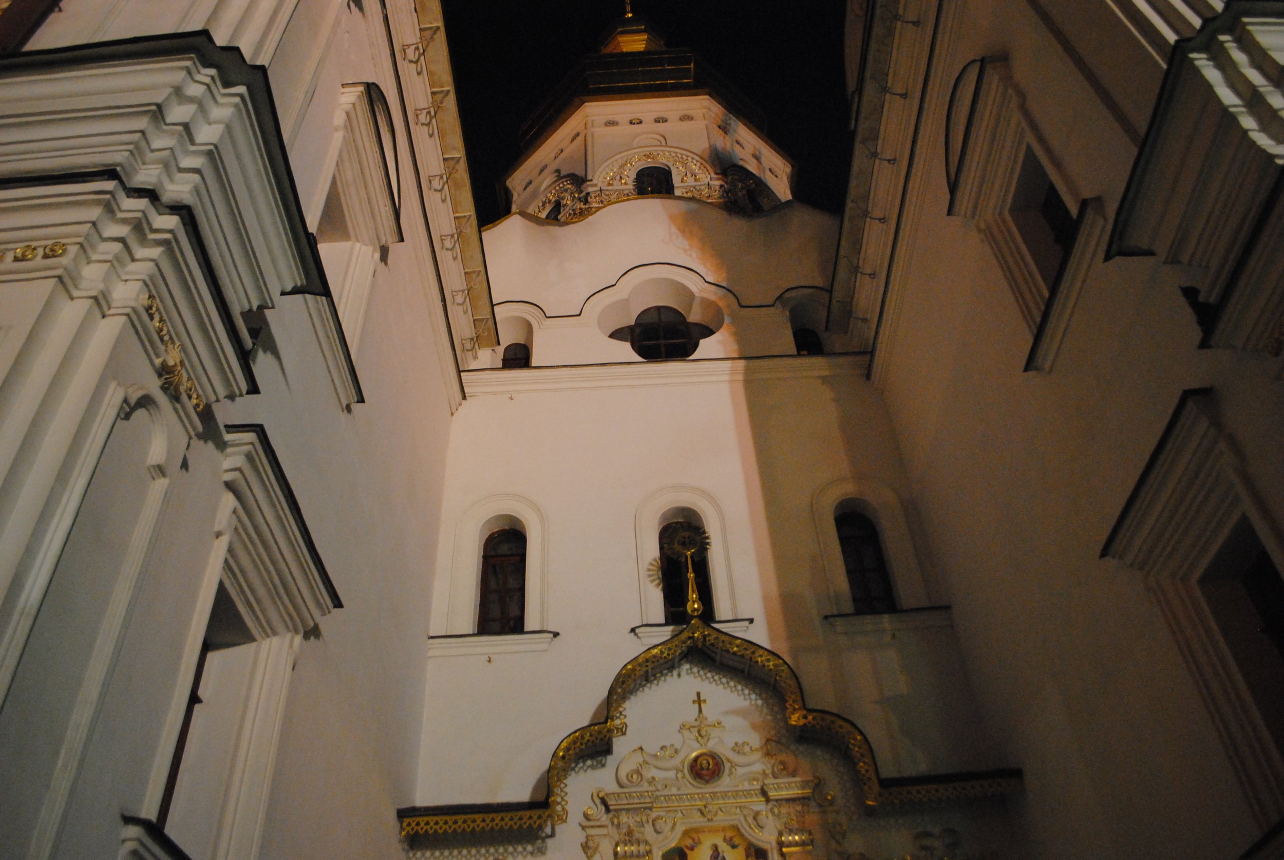 Night view of inside a church with ornate gold and white decorations, featuring an altar and religious icons.