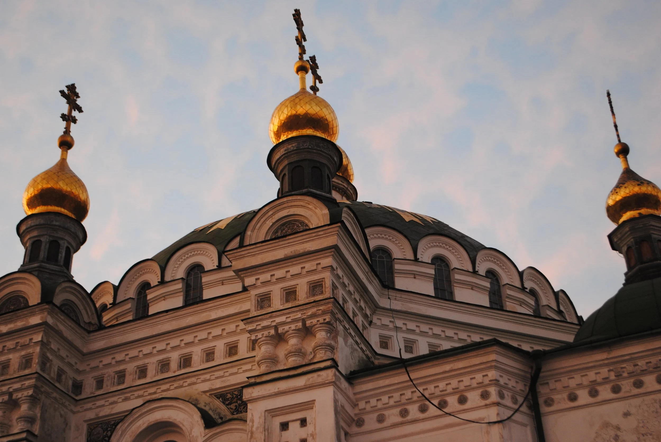 Orthodox church with golden onion domes and crosses on top, ornate architectural details, set against a blue sky with scattered clouds.