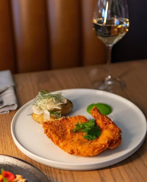 Fried fish fillet garnished with cilantro, served with green sauce, accompanied by a dollop of coleslaw with dill on a white plate