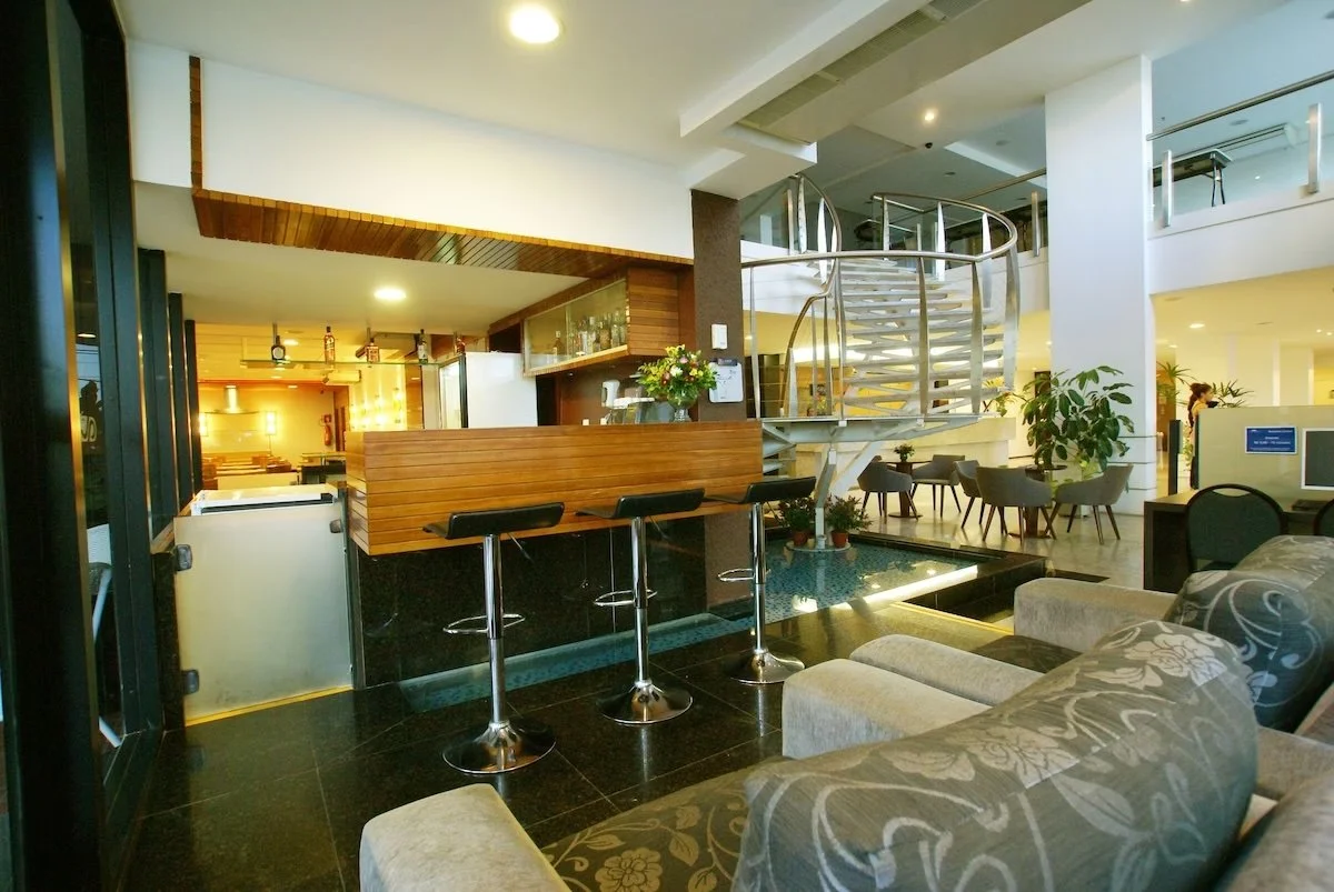 Interior of a modern hotel lobby with a reception desk, a spiral staircase, seating area with chairs and sofas, and decorative plants.